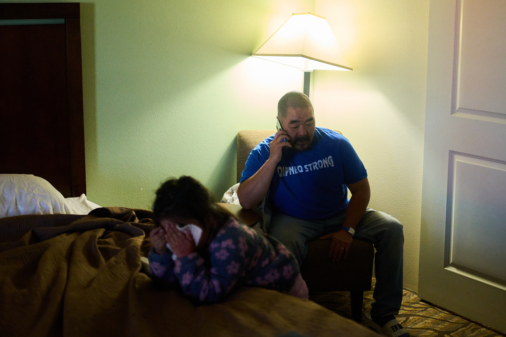 Darrell John speaks on the phone alongside his daughter Emi in the single hotel room his family is sharing in Anchorage, Alaska, Wednesday, Oct. 29, 2025, after losing their home in Kipnuk due to Typhoon Halong earlier in the month. (AP Photo/Lindsey Wasson)