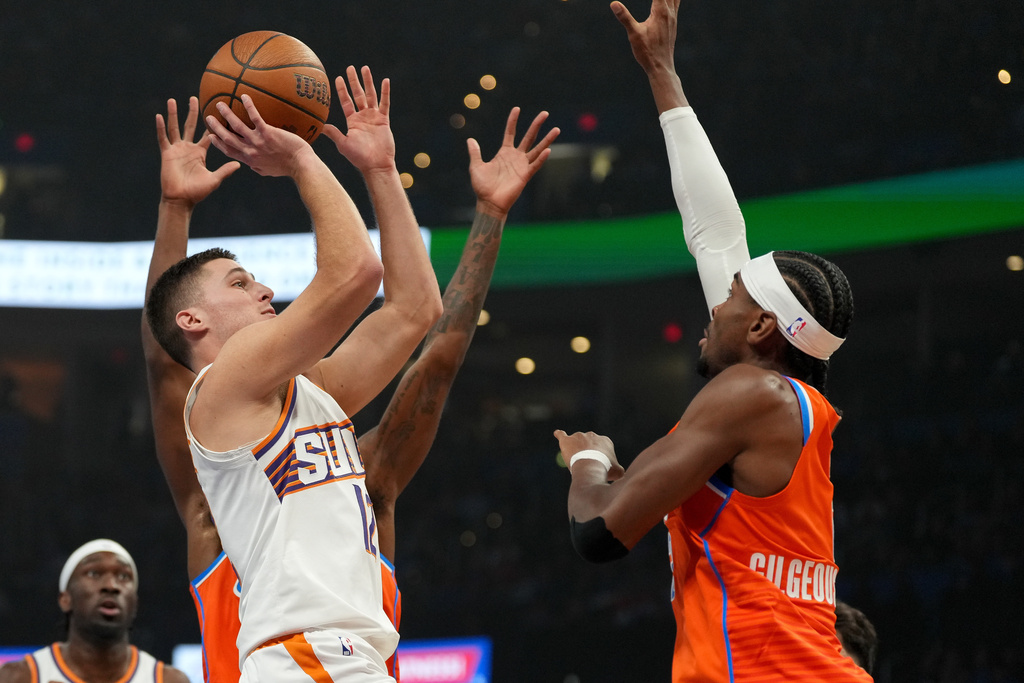 Phoenix Suns guard Collin Gillespie, left, shoots over Oklahoma City Thunder guard Shai Gilgeous-Alexander during the first half of an NBA Cup basketball game, Wednesday, Dec. 10, 2025, in Oklahoma City. (AP Photo/Kyle Phillips)