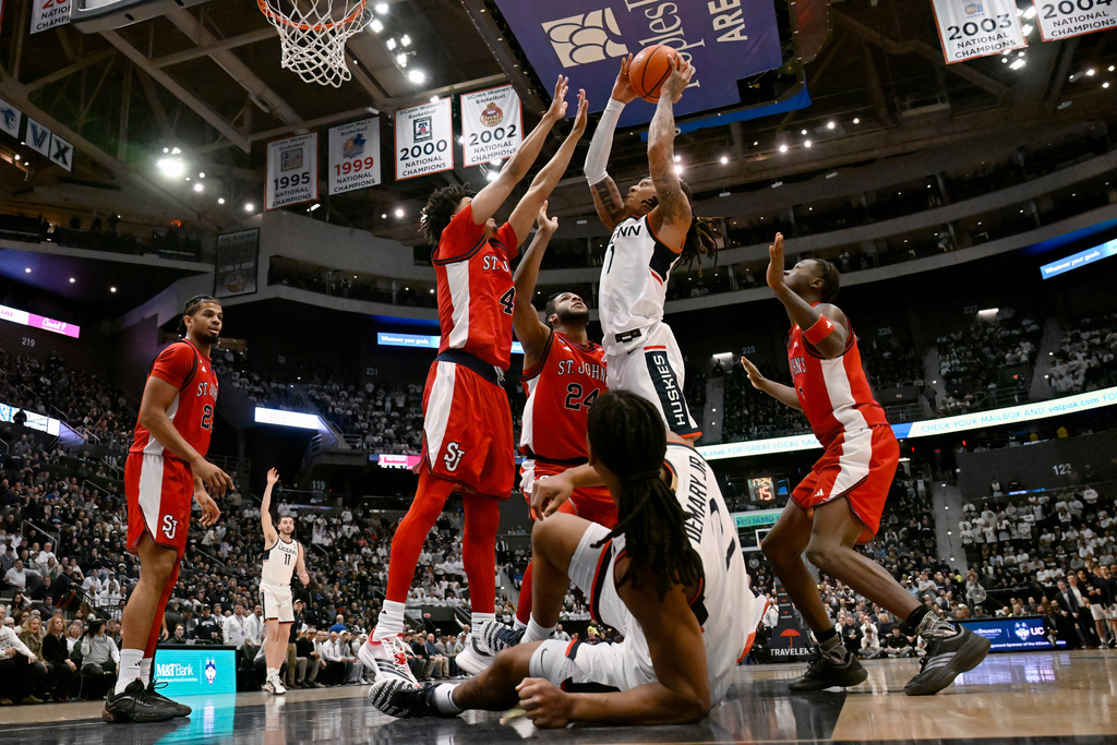 UConn guard Solo Ball (1) shoots while guarded by St. John's guard Oziyah Sellers (4) and St. John's forward Zuby Ejiofor (24) in the first half of an NCAA college basketball game, Wednesday, Feb. 25, 2026, in Hartford, Conn. (AP Photo/Jessica Hill)