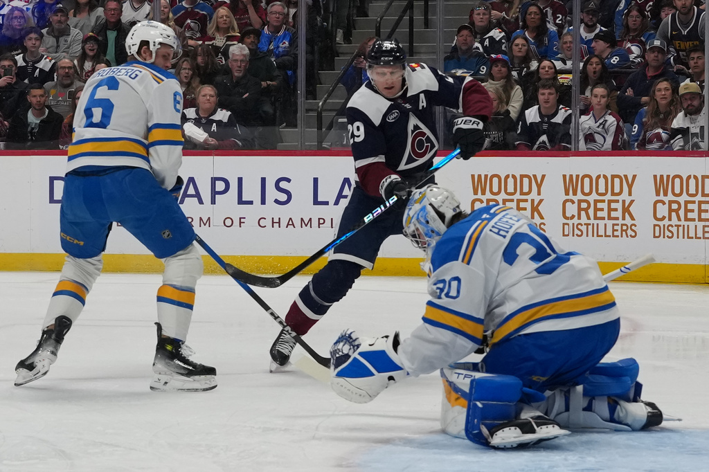 St. Louis Blues goaltender Joel Hofer, right, makes a glove save of a shot by Colorado Avalanche center Nathan MacKinnon as St. Louis defenseman Philip Broberg covers in the first period of an NHL hockey game Sunday, April 5, 2026, in Denver. (AP Photo/David Zalubowski)