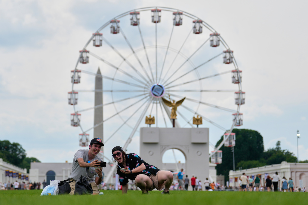 Christine Bayly, right, and Jason Brown, left, take a photo as they eat lunch on the National Mall with the Washington Monument, Freedom 250 Ferris Wheel, and a replica of the triumphal arch, behind them during the Great American State Fair, Friday, June 26, 2026, in Washington. (AP Photo/Carolyn Kaster)