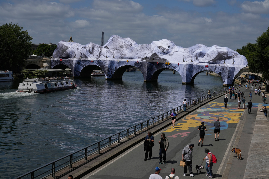 People walk along the Seine river next to "The Pont Neuf Cave," an inflated art installation by French street artist JR, on Paris' oldest bridge, the Pont Neuf, Thursday, May 21, 2026, which will be open to the public from June 6-28. (AP Photo/Michel Euler)