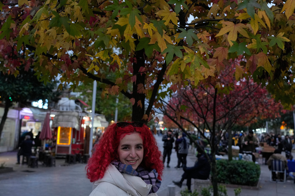 A woman smiles under a colourful tree in the northern city of Rasht, Iran, on Friday, Dec. 26, 2025. (AP Photo/Vahid Salemi)