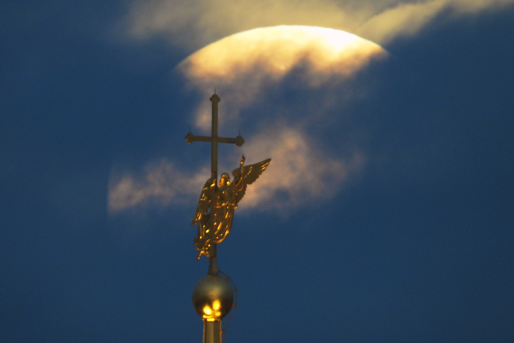 The Harvest Supermoon sets in the clouds behind the city landmark, a weather vane in the form of an angel fixed atop a spire of the Saints Peter and Paul Cathedral in St. Petersburg, Russia, early Tuesday, Oct. 7, 2025. (AP Photo/Dmitri Lovetsky)