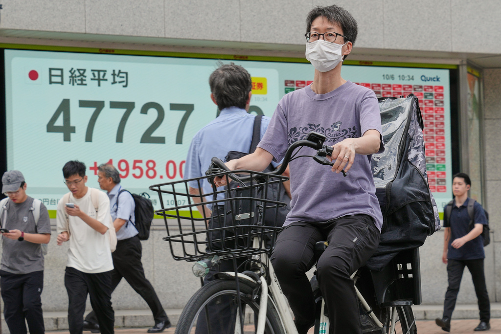 A person rides a bicycle in front of an electronic stock board showing Japan's Nikkei index at a securities firm Monday, Oct. 6, 2025, in Tokyo. (AP Photo/Eugene Hoshiko)