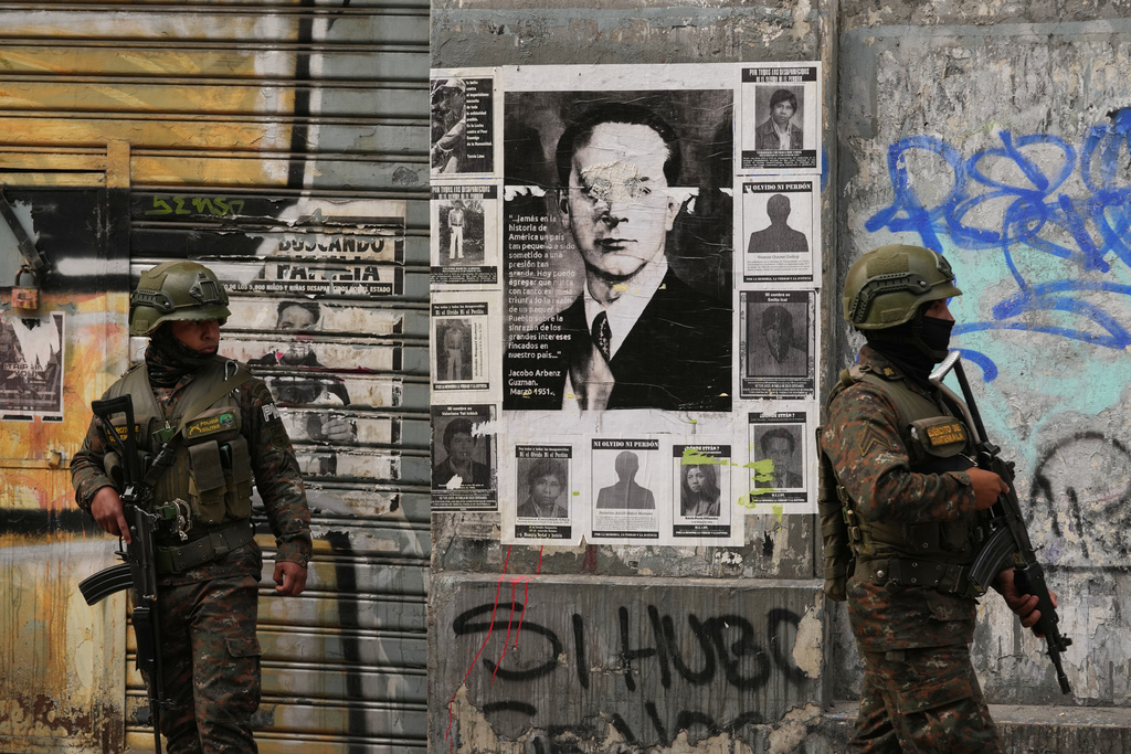 Soldiers stand guard in front of a poster of former President Jacobo Arbenz who was overthrown in a 1954 coup, near Congress in Guatemala City, Monday, Jan. 19, 2026, after President Bernardo Arévalo declared a state of emergency. (AP Photo/Moises Castillo)