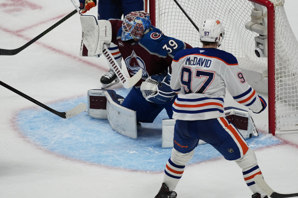 Edmonton Oilers center Connor McDavid, front, scores a power-play goal against Colorado Avalanche goaltender MacKenzie Blackwood in the third period of an NHL hockey game Tuesday, March 10, 2026, in Denver. (AP Photo/David Zalubowski)