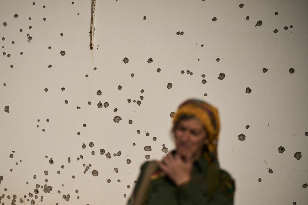 A member of the armed wing of the Kurdish-Iranian opposition group Organization of Iranian Kurdistan Struggle, known as Khabat, stands in front of a shrapnel pockmarked wall that allegedly was damaged in strike by Iranian-backed militias in Iraq last week at a military base on the outskirts of Irbil, Iraq, Monday, March 16, 2026. (AP Photo/Leo Correa)