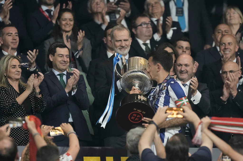 Spain's King Felipe VI, centre, looks as Real Sociedad's Mikel Oyarzabal kisses the trophy after the Copa del Rey final soccer match between Atletico Madrid and Real Sociedad in Seville, Spain, Saturday, April. 18, 2026. (AP Photo/Jose Breton)