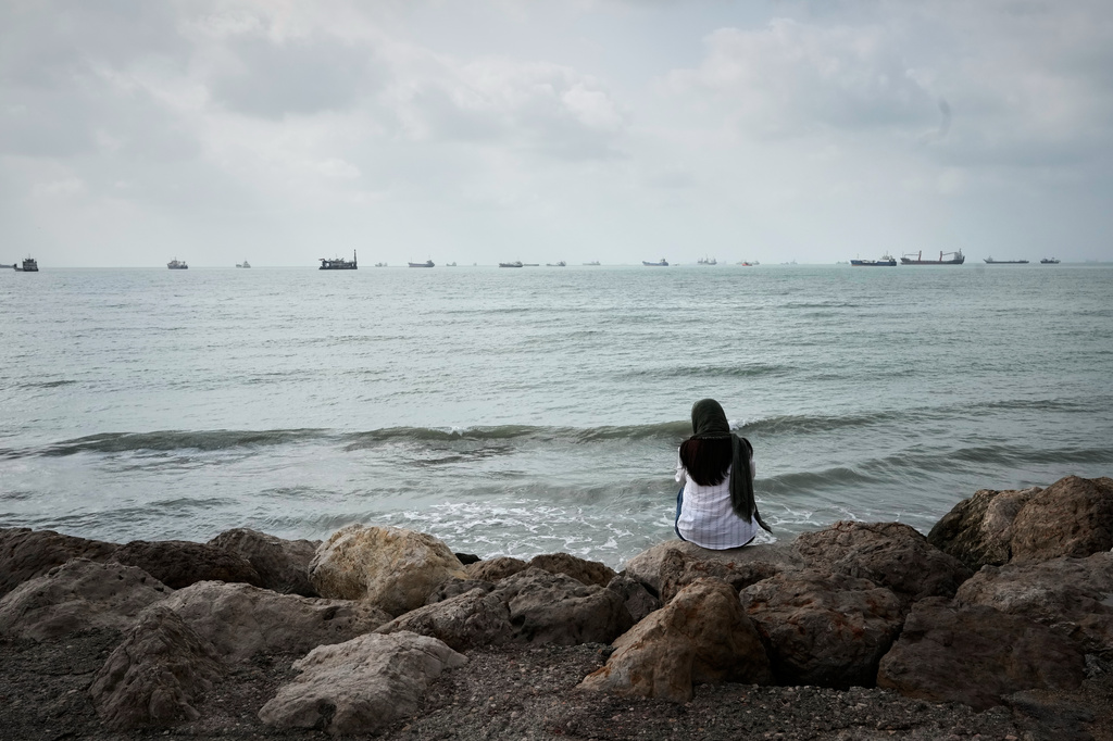 A woman relaxes along the rocky shoreline as commercial vessels lie anchored off Bandar Abbas, Iran, Friday, Sept. 4, 2026. (AP Photo/Vahid Salemi)