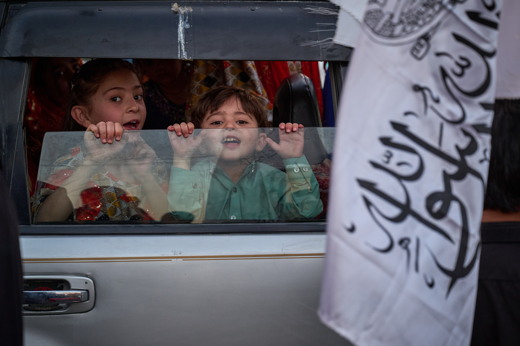 Young children look out from a car as a Taliban flag is held nearby on the eve of the fifth anniversary of the U.S. withdrawal and the start of Taliban rule in Kabul, Afghanistan, Friday, Aug. 14, 2026. (AP Photo/Nava Jamshidi)
