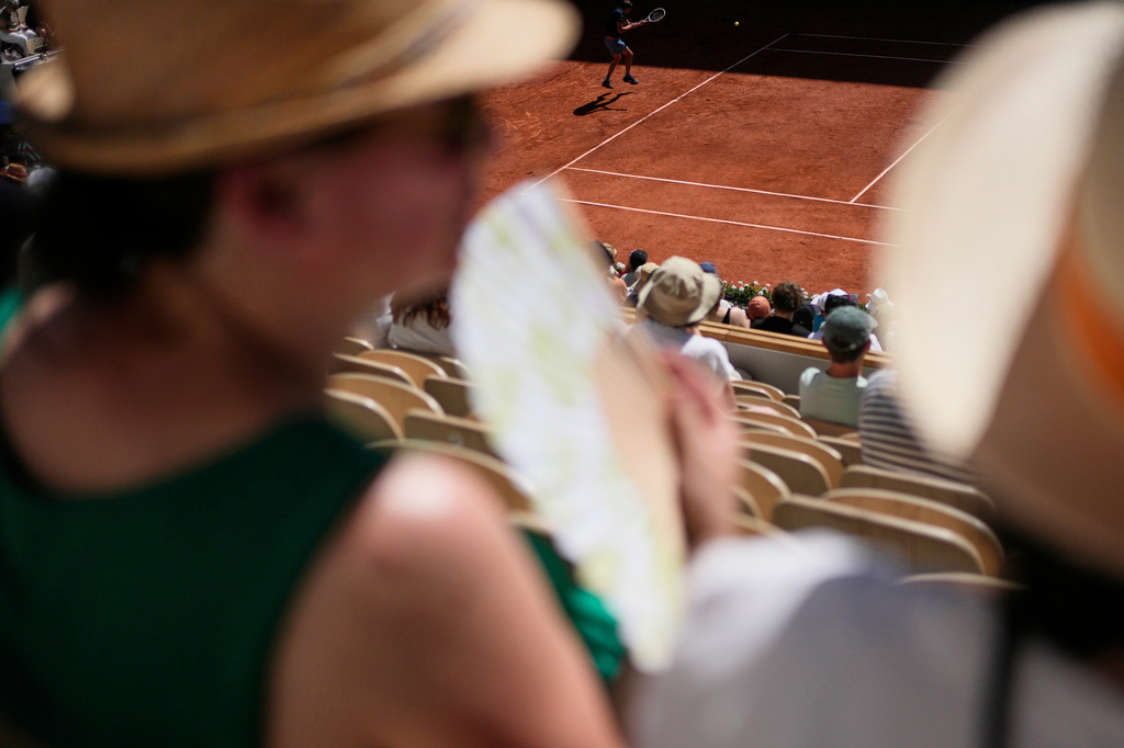Spectators cool themselves with hand fans as Daniil Medvedev of Russia, top, returns to Adam Walton of Australia during their first round men's singles tennis match at the French Open tennis tournament in Paris, Tuesday, May 26, 2026. (AP Photo/Christophe Ena)