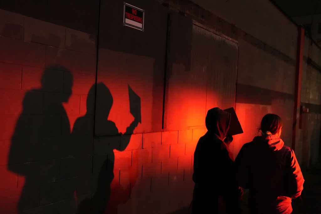 Two protesters are lit by a police light as they walk outside the U.S. Immigration and Customs Enforcement facility on Thursday, Jan. 8, 2026, in Portland, Ore. (AP Photo/Jenny Kane)