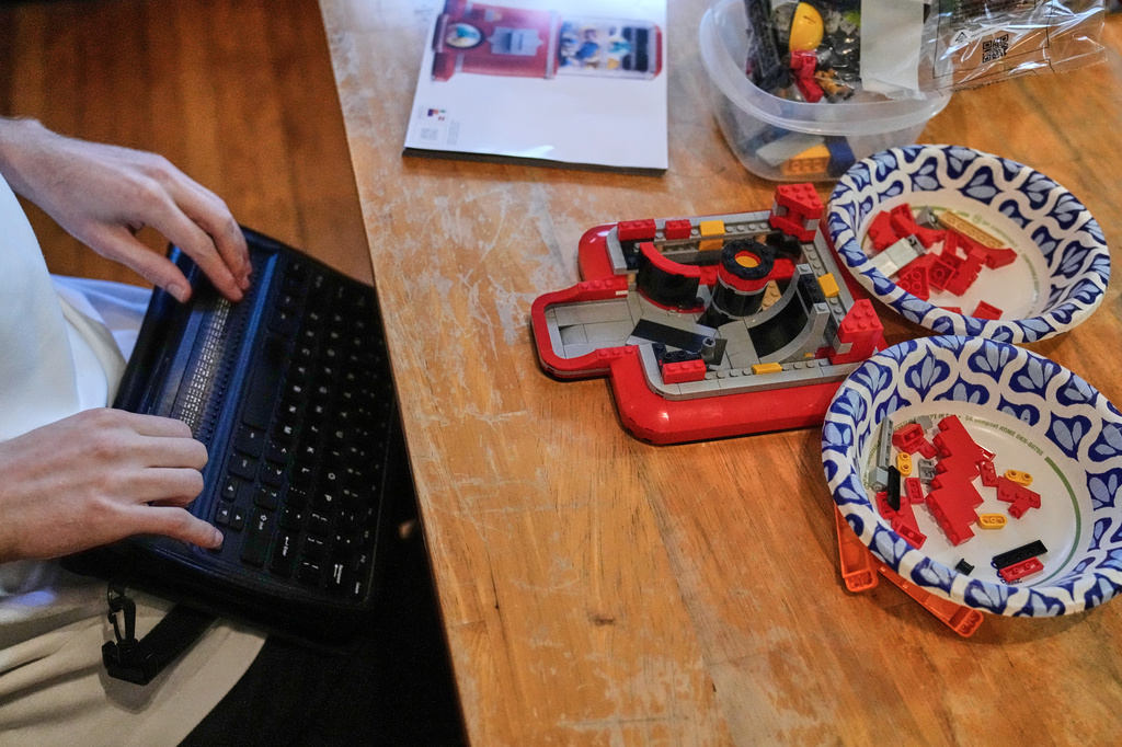 Matthew Shifrin, the founder of Bricks for the Blind, reads from a braille terminal while building a LEGO gum ball machine at his family's home, Friday, March 20, 2026, in Newton, Mass. (AP Photo/Charles Krupa)