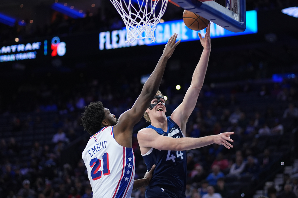 Minnesota Timberwolves' Rocco Zikarsky, right, goes up for a shot past Philadelphia 76ers' Joel Embiid during the first half of a preseason NBA basketball game Friday, Oct. 17, 2025, in Philadelphia. (AP Photo/Matt Slocum)