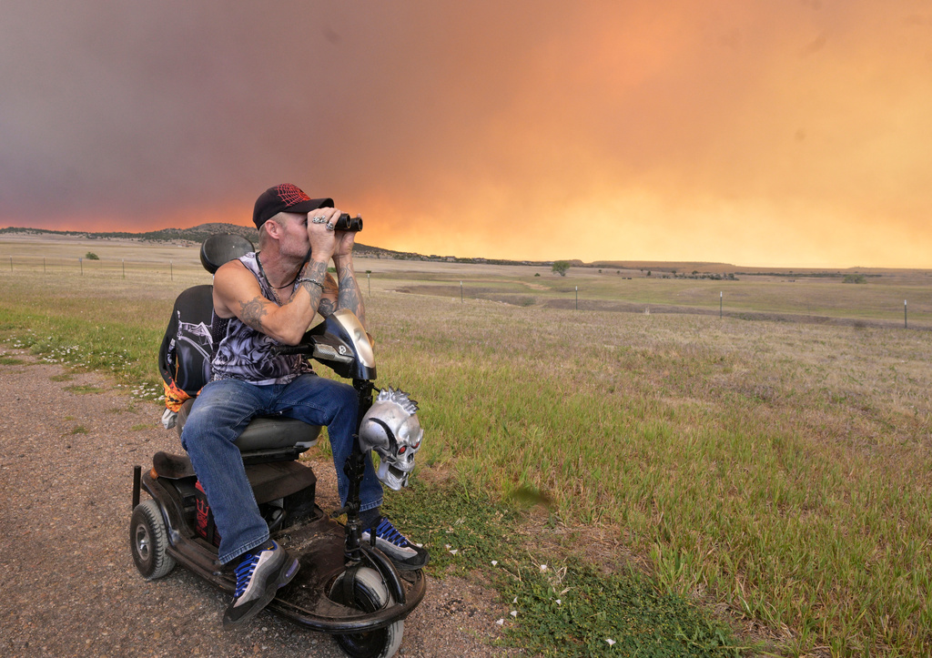 Justin Burk looks through binoculars from a road near his home in Mountain Shadows Mobile Estates, at the Aspen Acres Fire near Beulah, Colo., Monday, June 29, 2026. (Jerilee Bennett/The Gazette via AP)