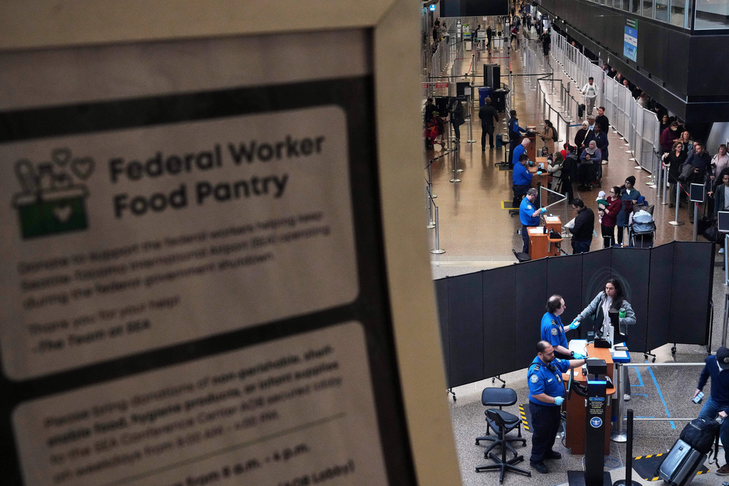 A sign for a food pantry for federal workers is seen as TSA agents check identification at a security checkpoint at Seattle-Tacoma International Airport, Thursday, Nov. 6, 2025, in SeaTac, Wash. (AP Photo/Lindsey Wasson)