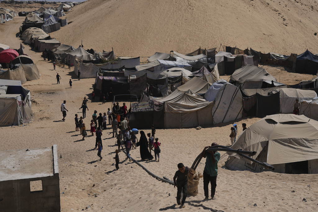 Displaced Palestinians walks through a tent camp in Muwasi, an area that Israel has designated as a safe zone, in Khan Younis southern Gaza Strip, Sunday, Sept. 21, 2025. (AP Photo/Jehad Alshrafi)