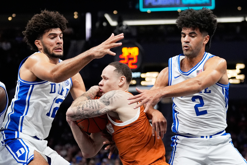 Texas guard Chendall Weaver drives to the basket between Duke forward Cameron Boozer, left, and guard Cayden Boozer during the first half of an NCAA college basketball game, Tuesday, Nov. 4, 2025, in Charlotte, N.C. (AP Photo/Chris Carlson)