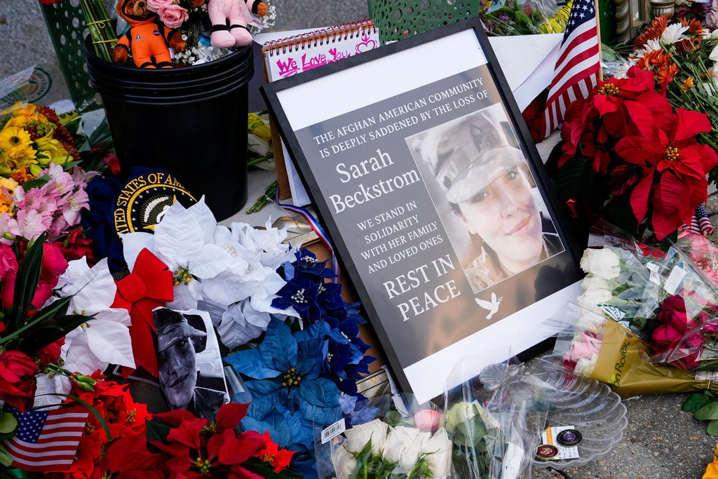 Flowers, challenge coins and other items lay near a photograph of U.S. Army Spc. Sarah Beckstrom at a makeshift memorial outside of Farragut West Station, near the site where two National Guard members were shot, Monday, Dec. 1, 2025, in Washington. (AP Photo/Julia Demaree Nikhinson)