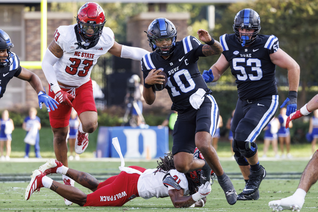 Duke's Darian Mensah (10) carries the ball as North Carolina State's Jamel Johnson (21) and Kenny Soares, Jr. (33) pursue during the first half of an NCAA college football game in Durham, N.C., Saturday, Sept. 20, 2025. (AP Photo/Ben McKeown)