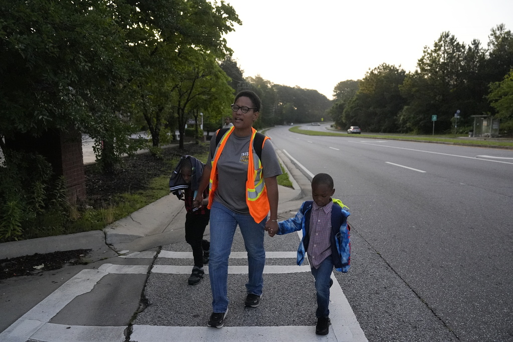 Sechita McNair, center, and sons Derrick McNair-White, 6, left, and Malachi McNair-Nesbitt, 6, right, walk near a busy street to catch a city bus on June 11, 2025, in Jonesboro, Ga. (AP Photo/Brynn Anderson)
