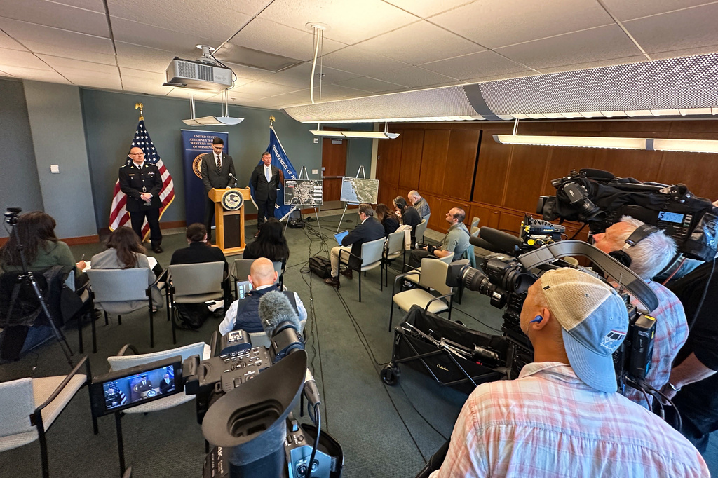 In this photo taken with a smartphone, Mike Herrington, the FBI special agent in charge, speaks to the media on Tuesday, Oct. 6, 2026, in Seattle. Standing next to Herrington are Elija Rain, the assistant commissioner of the British Columbia Royal Canadian Mounted Police, left, and Acting U.S. Attorney Neil Floyd, right. (AP Photo/Manuel Valdes)