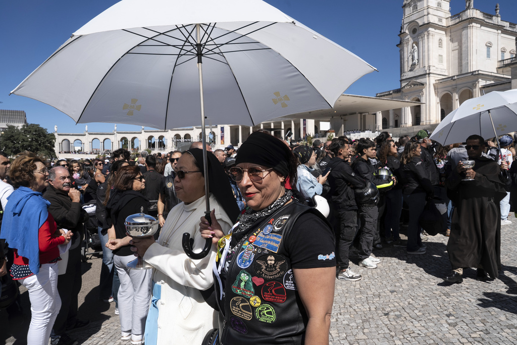 A motorcyclist holds an umbrella for nun carrying a communion wafer box at the Roman Catholic holy shrine of Fatima, during the 10th Pilgrimage of the Blessing of Helmets that draws tens of thousands, in Fatima, Portugal, Sunday, Sept. 21, 2025. (AP Photo/Ana Brigida)
