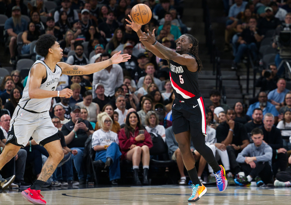 Portland Trail Blazers guard Jrue Holiday (5) grabs the ball ahead of San Antonio Spurs guard Dylan Harper during the first half of an NBA basketball game, Wednesday, April 8, 2026, in San Antonio. (AP Photo/Darren Abate)