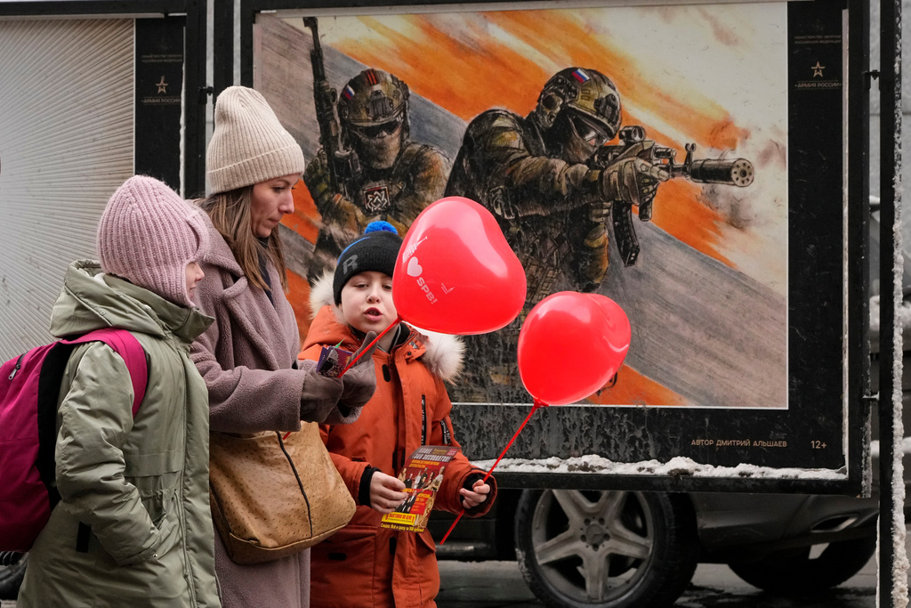 FILE - A woman with two children walks past a street exhibition of military posters named 'Together to Victory' dedicated to Russian army in St. Petersburg, Russia, Friday, Feb. 14, 2025. (AP Photo/Dmitri Lovetsky, File)