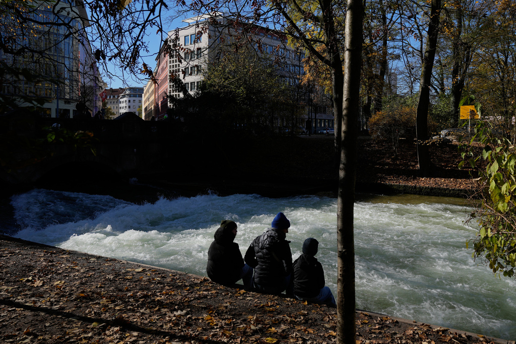 People sit at the Eisbach, where the famous wave usually forms, in Munich, Germany, Wednesday, Nov. 5, 2025. (AP Photo/Matthias Schrader)