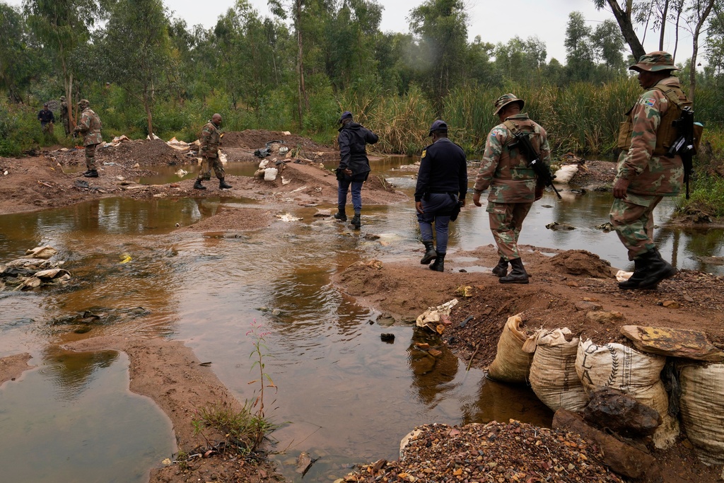 South African National Defense Force soldiers and police officers cross a water stream used by illegal miners, during a patrol in Randfontein, in Johannesburg, South Africa, Thursday, March 12, 2026. (AP Photo/Themba Hadebe)