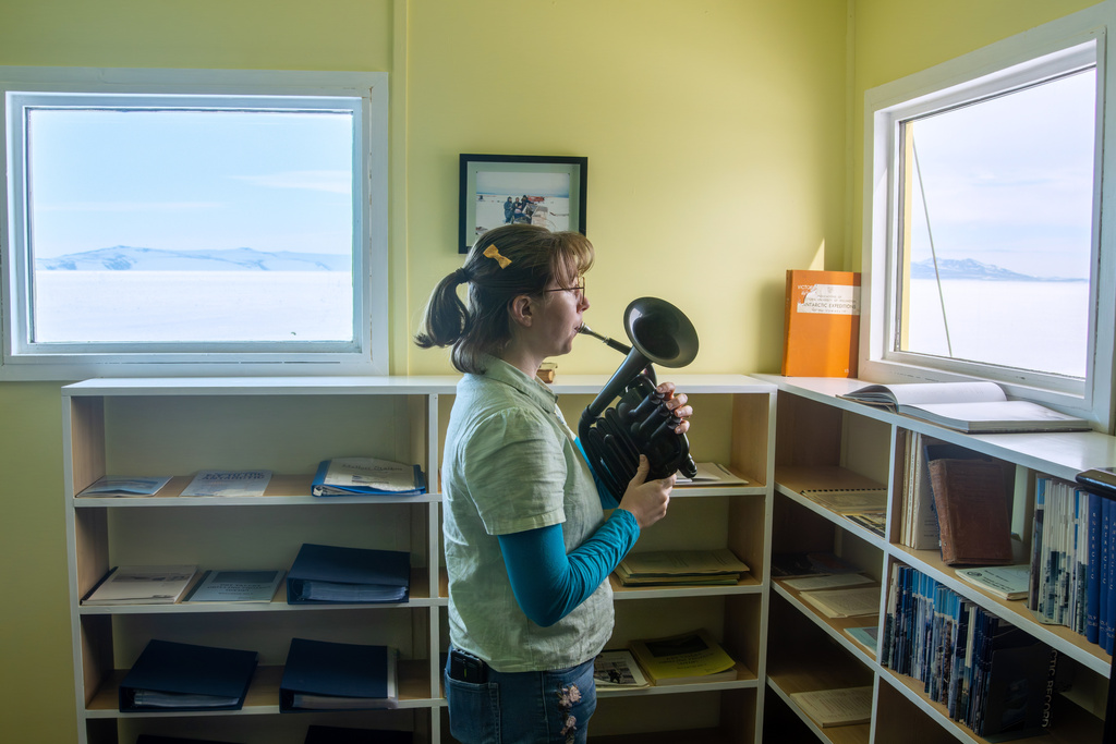 In this photo provided by Antarctica New Zealand, Natalie Paine plays a plastic French horn at Scott Base in Antarctica, on Nov. 16, 2025. (Anthony Powell/Antarctica New Zealand via AP)