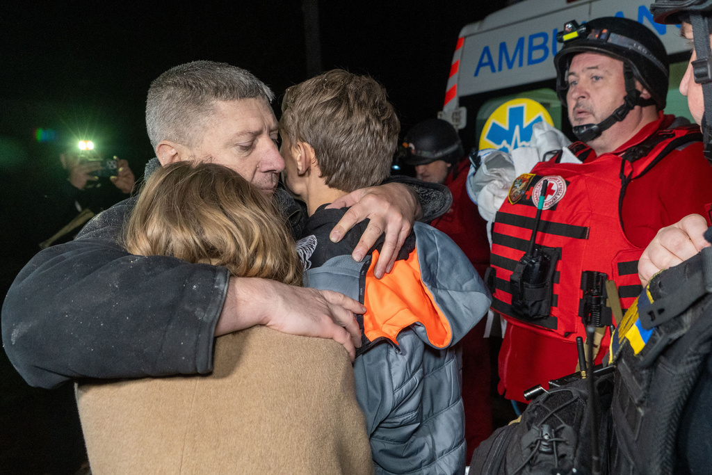 A man hugs his children as they react to the death of their mother killed by a Russian airstrike in Kharkiv, Ukraine, late Sunday, Nov. 23, 2025. (AP Photo/Andrii Marienko)