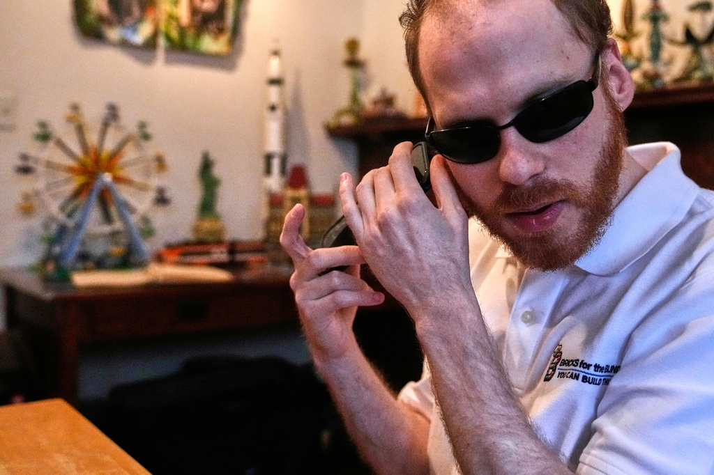 Matthew Shifrin, the founder of Bricks for the Blind, listens to directions on his phone while building a LEGO gum ball machine at his family's home, Friday, March 20, 2026, in Newton, Mass. (AP Photo/Charles Krupa)