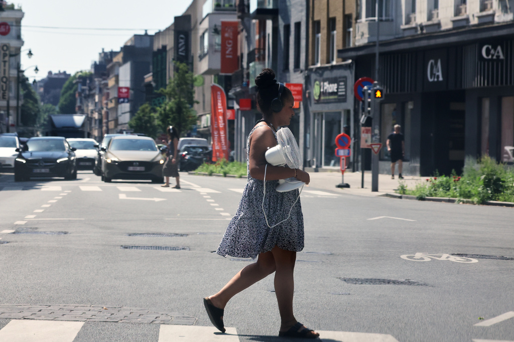 A woman walks across the street with a fan in her arms in the center of Brussels, Thursday, June 25, 2026. (AP Photo/Omar Havana)