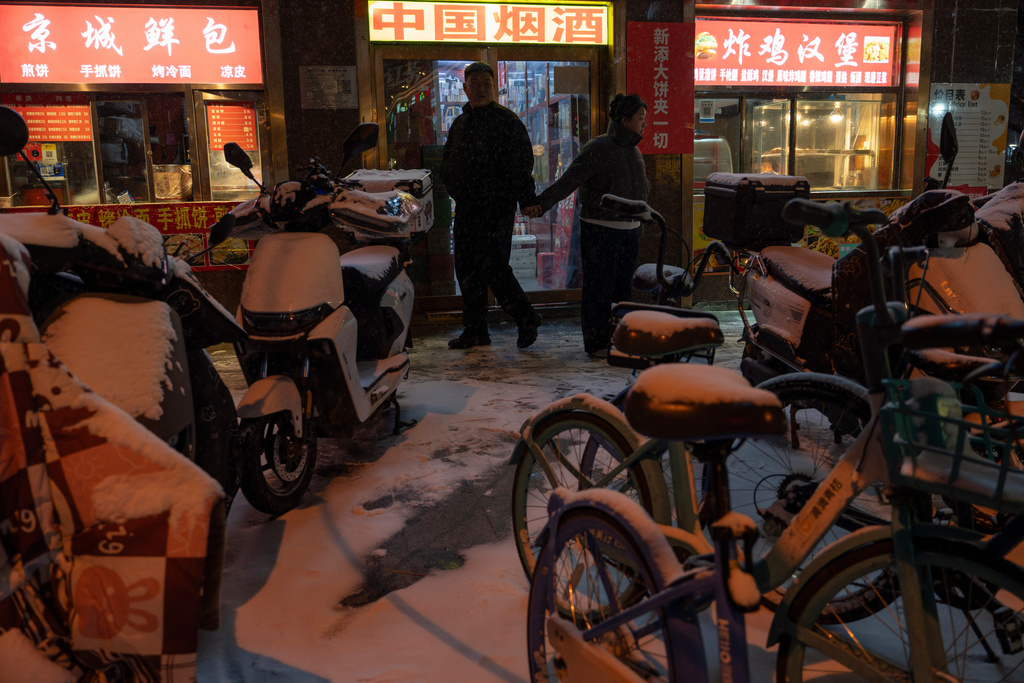 A couple walks near neighborhood stores in Beijing, Friday, Dec. 12, 2025. (AP Photo/Ng Han Guan)