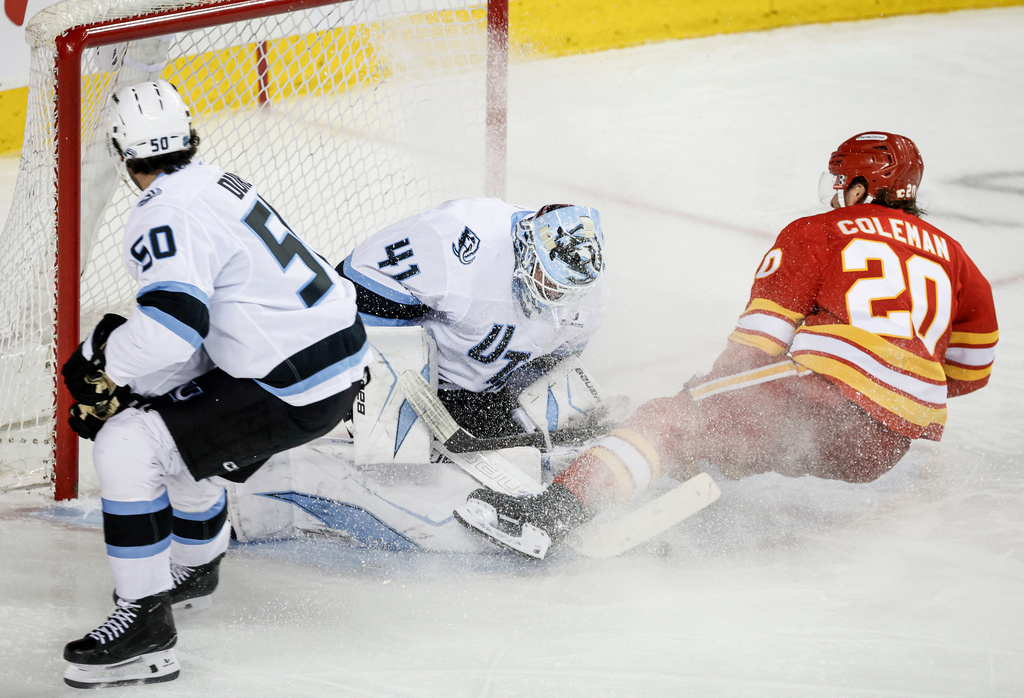 Utah Mammoth goalie Vitek Vanecek, center, lets in a goal from Calgary Flames' Blake Coleman, right, as Sean Durzi looks on during the third period of an NHL hockey game in Calgary on Sunday, April 12, 2026. (Jeff McIntosh/The Canadian Press via AP)
