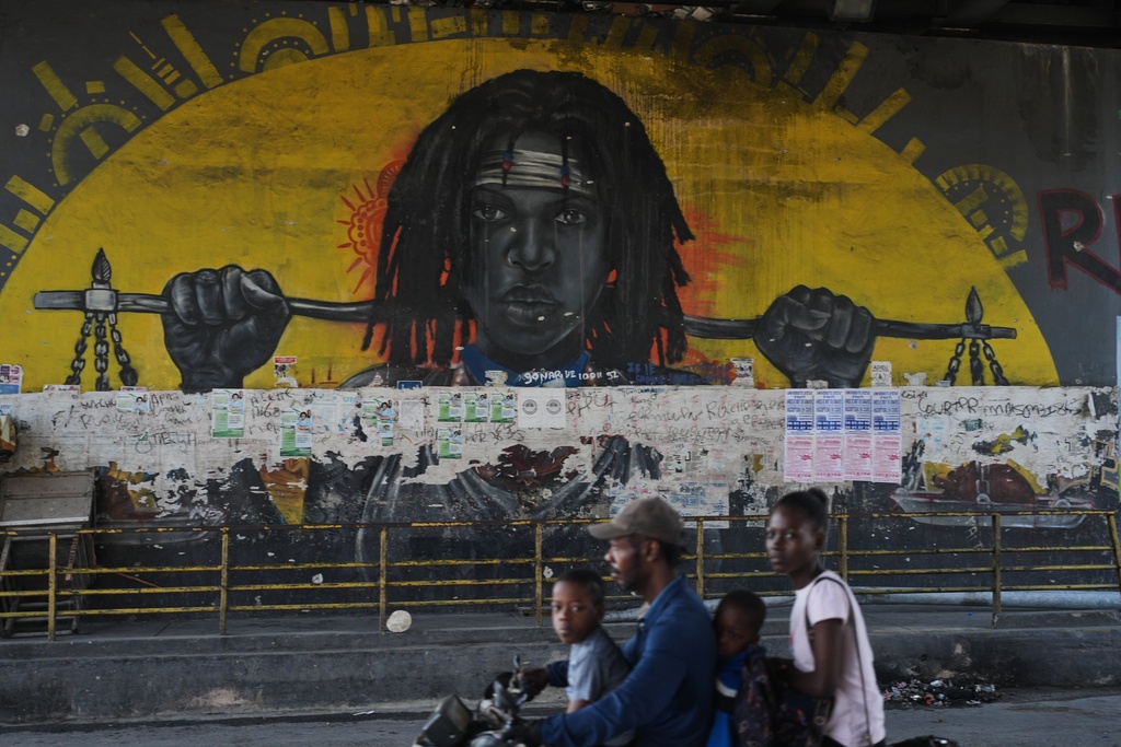 A moto taxi driver rides past a mural under a bridge at the Carrefour Aeoport intersection in the Delmas community of the district of Port-au-Prince, Haiti, Tuesday, Feb. 24, 2026. (AP Photo/Odelyn Joseph)