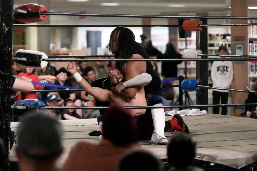 Fans watch as wrestler Elliot Rey, middle top, applies a hold on TJ Black during a Lucha Libro pro wrestling event at Benicia Public Library Saturday, May 2, 2026, in Benicia, Calif. (AP Photo/Jeff Chiu)