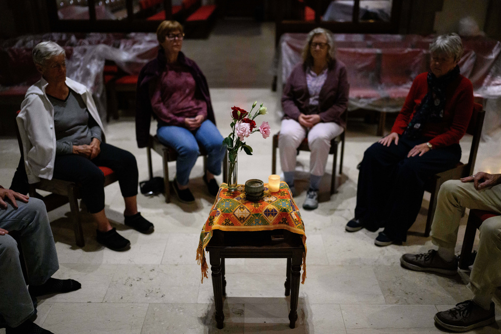 People sit around a table with an orange tapestry gifted by Himalayan refugees, an incense bowl, flowers and a candle during an interfaith meditation practice at All Saints Episcopal Church in Pasadena, Calif., on Monday, Dec. 15, 2025. (AP Photo/William Liang)