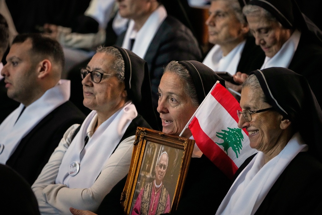 A nun holds a Lebanese flag and a portrait of Pope Leo XIV as he gathers with worshippers at the Catholic basilica of Harissa, Lebanon, Monday, Dec. 1, 2025. (AP Photo/Hussein Malla)