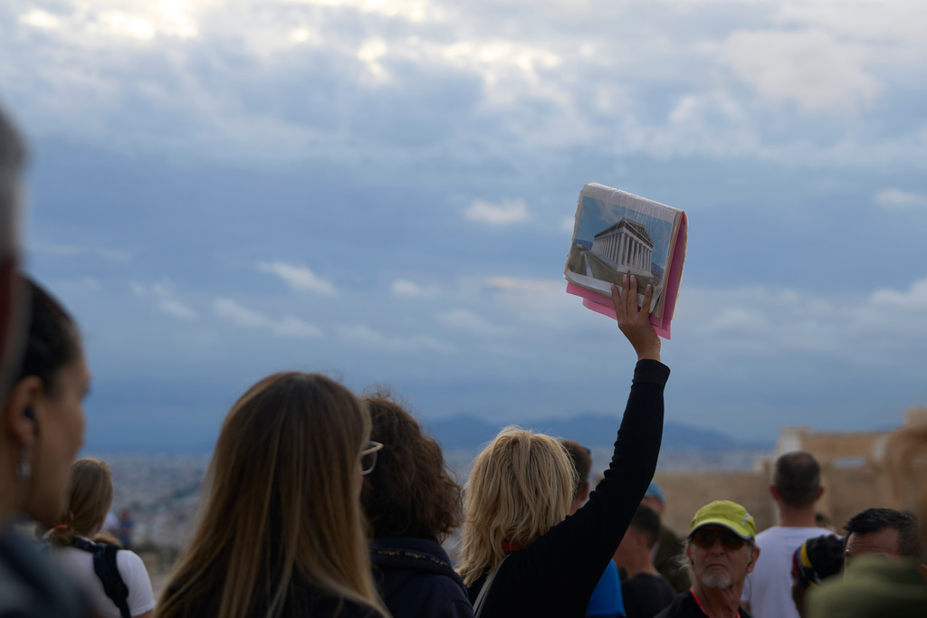 A tourist guide holds an illustration of the historical 5th century B.C. Parthenon temple as she speaks to a group atop the Acropolis hill in Athens, Friday, Oct. 31, 2025. (AP Photo/Petros Giannakouris)