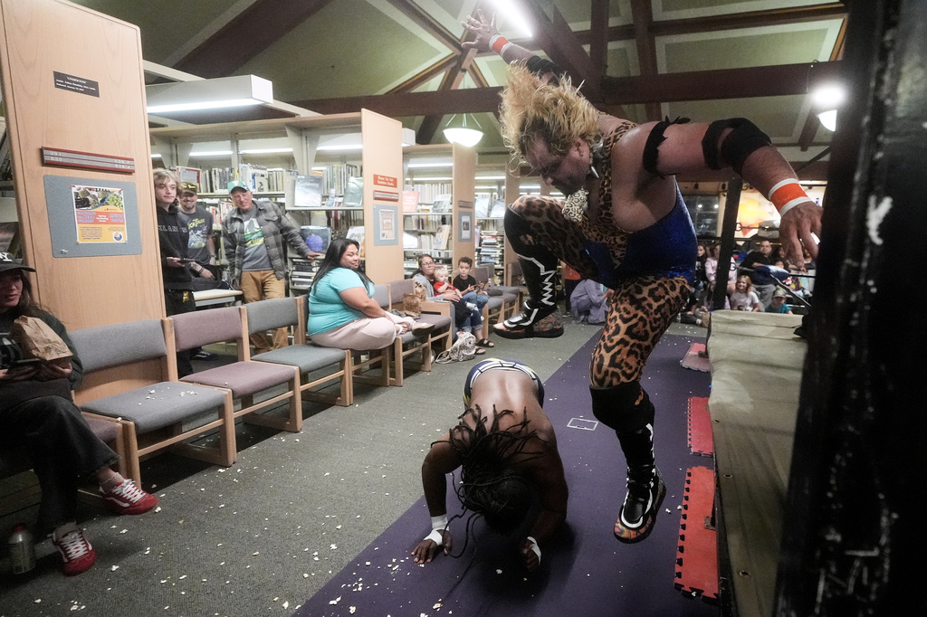 Fans watch as wrestler Jaguar Montoya, top, stomps on OC Hayes outside of the ring during a Lucha Libro pro wrestling event at Benicia Public Library Saturday, May 2, 2026, in Benicia, Calif. (AP Photo/Jeff Chiu)