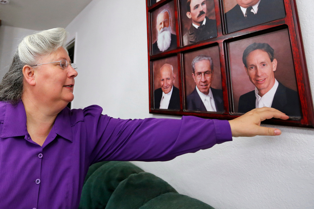FILE - Norma Richter points to a collection of portraits of prophets of the Fundamentalist Church of Jesus Christ of Latter-Day Saints, including Warren Jeffs, bottom right, on a wall at her home in a community on the Utah-Arizona border, Oct. 27, 2017. (AP Photo/Rick Bowmer, File)