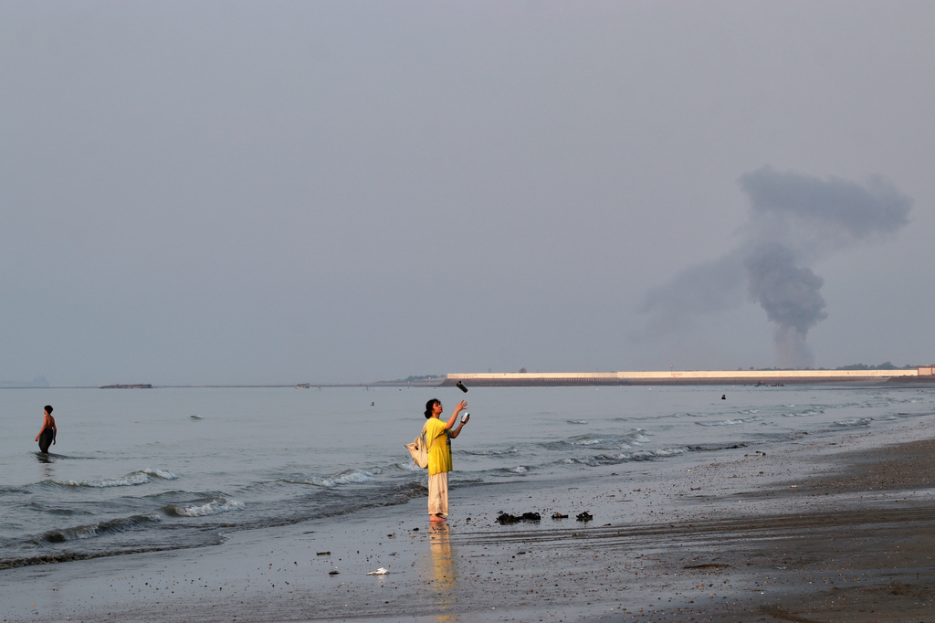 A woman stands at the water's edge along the Strait of Hormuz as a plume of smoke rises in the background following an explosion, off Bandar Abbas, Iran, Monday, July 13, 2026. (Razieh Poudat/ISNA via AP)