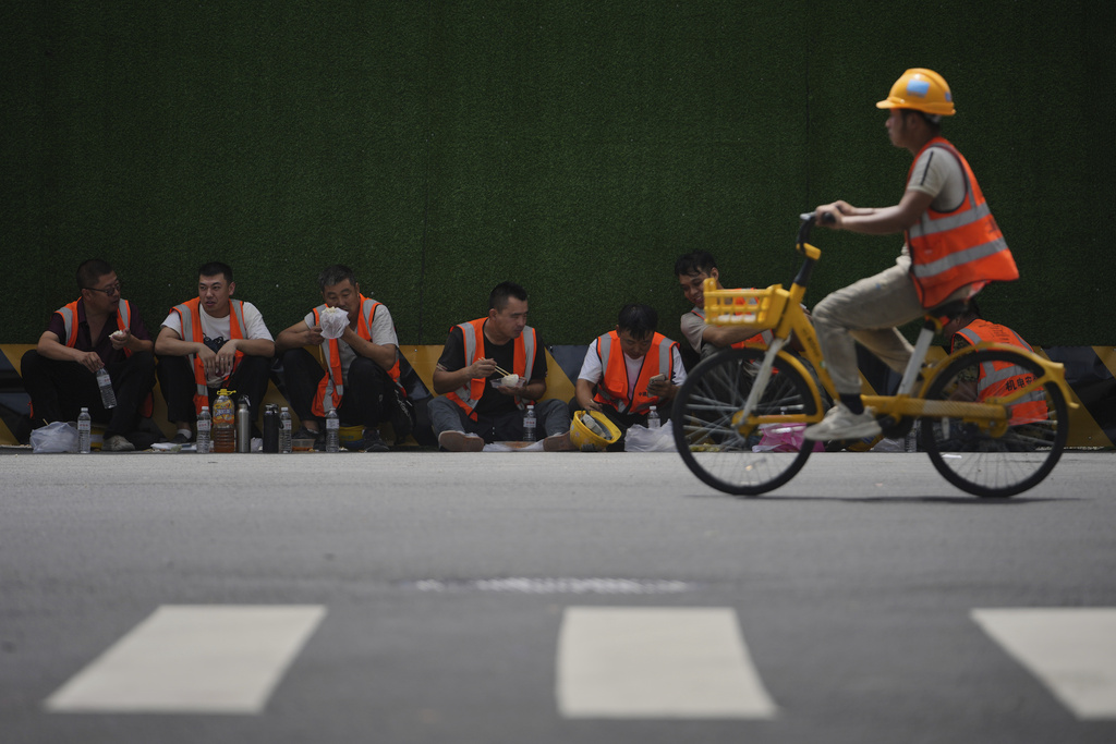 Construction workers eat their lunch along a road side near the office buildings at the central business district during lunch break hour in Beijing, Thursday, Aug. 7, 2025. (AP Photo/Andy Wong)
