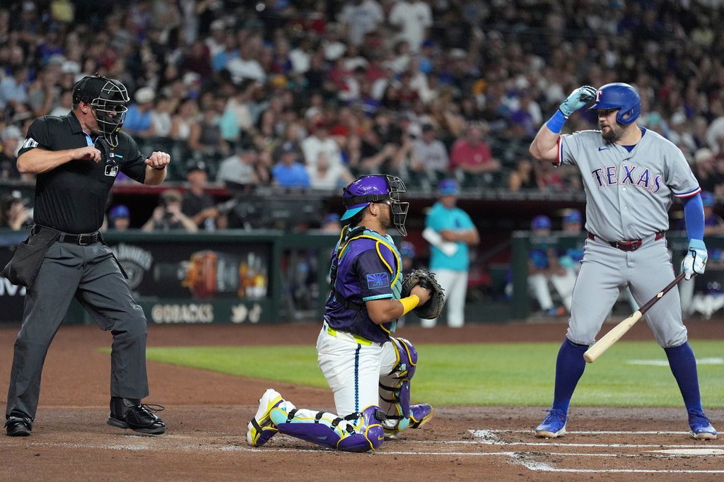 Texas Rangers'Jake Burger, right, challenges a called third strike by home plate umpire Brian Walsh, left, as Arizona Diamondbacks catcher Gabriel Moreno pauses at home plate, before the called was overturned, during the second inning of a baseball game, Friday, Sept. 11, 2026, in Phoenix. (AP Photo/Ross D. Franklin)