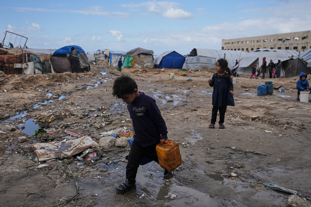 Palestinian children carry plastic jerrycans filled with water as they walk through a displacement camp in Gaza City, Sunday, Dec. 28, 2025. (AP Photo/Jehad Alshrafi)