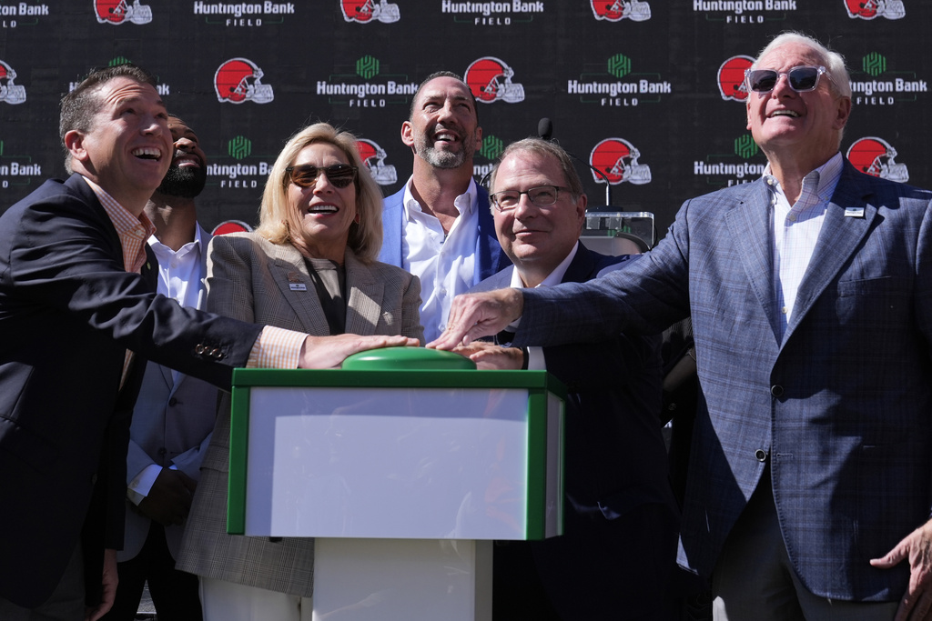 FILE - From left, Brant Standridge of Huntington Bank, Dee Haslam, Cleveland Browns owner, Steve Steinour of Huntington Bank and Jimmy Haslam, Cleveland Browns owner laugh after pressing a button to display "Huntington Bank Field" on the scoreboard at an NFL football news conference announcing Cleveland Browns Stadium will now be called Huntington Bank Field, on Sept. 3, 2024, in Cleveland. At rear is David Jenkins, Browns' chief operating officer. (AP Photo/Sue Ogrocki, File)